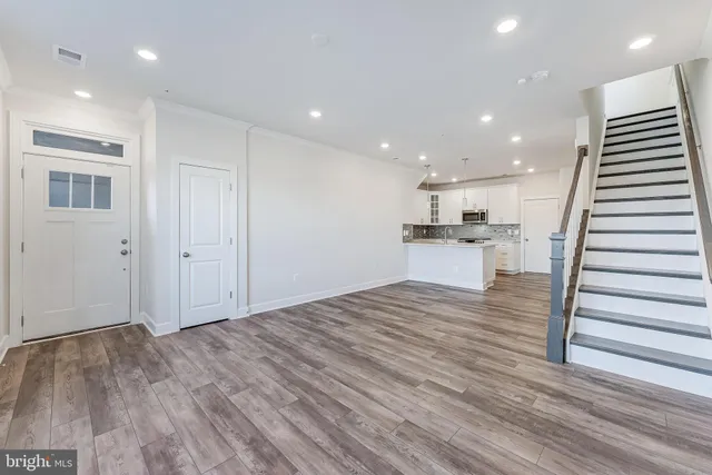an empty room with wooden floor and kitchen view