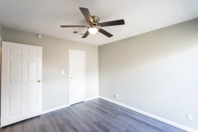 an empty room with wooden floor fan and windows