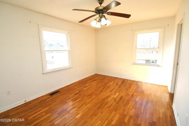 an empty room with wooden floor fan and windows