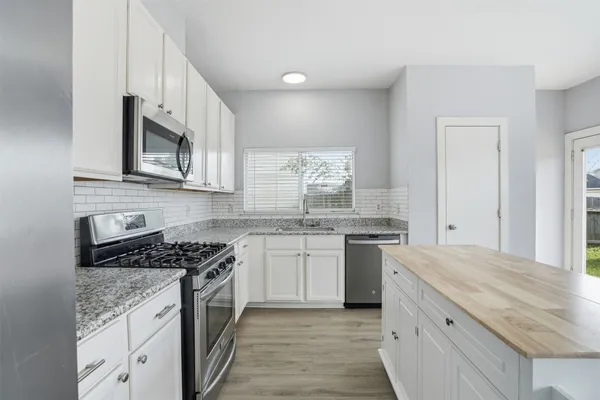 a kitchen with stainless steel appliances granite countertop a stove top oven a sink dishwasher and a microwave oven with white cabinets