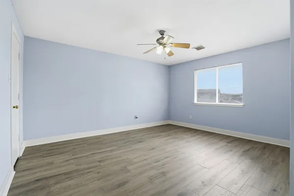 an empty room with wooden floor chandelier fan and windows