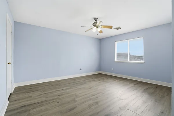 an empty room with wooden floor chandelier fan and windows