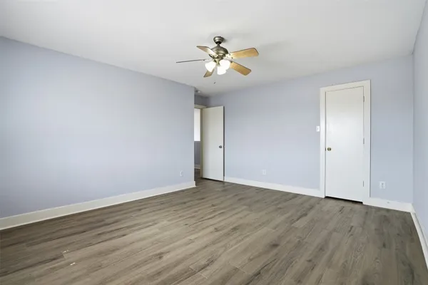 a view of an empty room with wooden floor and a ceiling fan