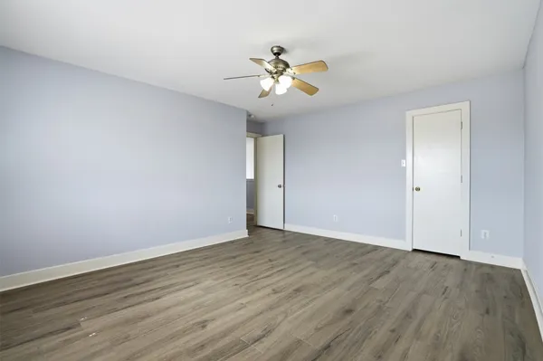 a view of an empty room with wooden floor and a ceiling fan