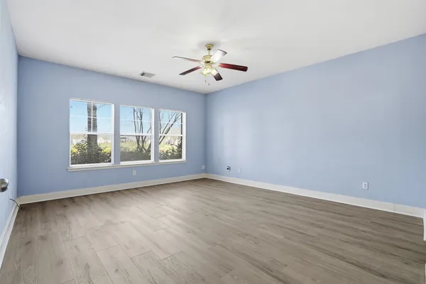 an empty room with wooden floor chandelier fan and windows