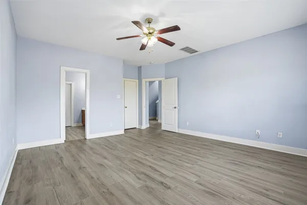 a view of an empty room with wooden floor and a ceiling fan