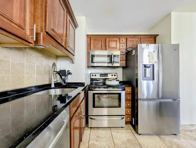 a kitchen with stainless steel appliances granite countertop a refrigerator a stove and a sink