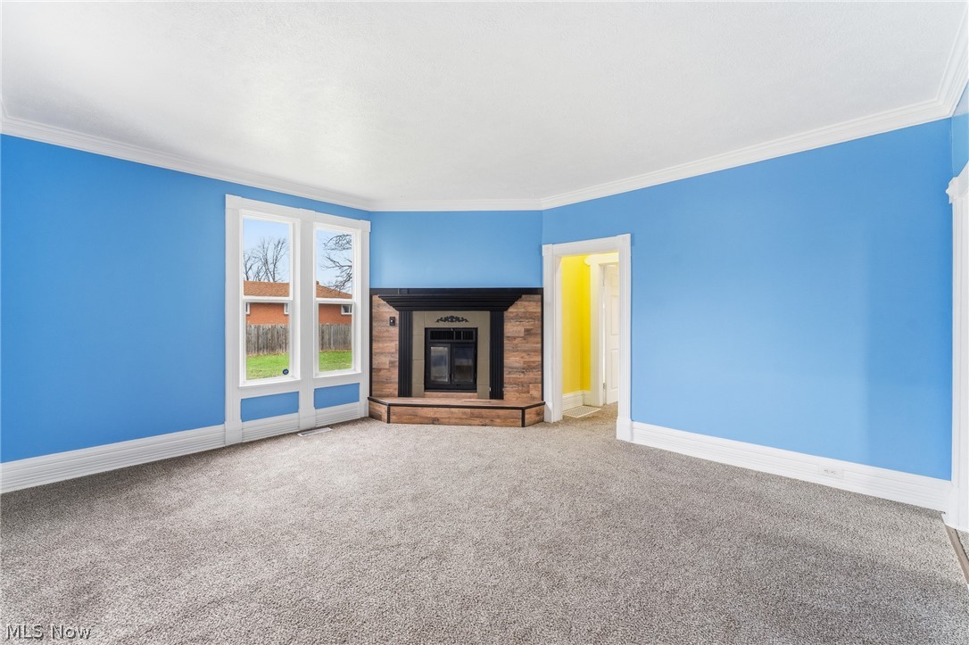 563 Geneva Avenue Struthers, OH 44471 - Photo 8 of 31 Unfurnished living room featuring a glass covered fireplace, carpet flooring, and ornamental molding