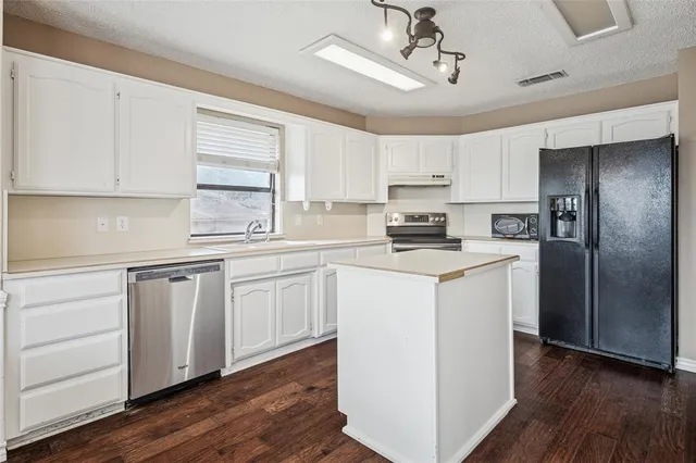 a kitchen with stainless steel appliances granite countertop a refrigerator a sink dishwasher a stove top oven a refrigerator and white cabinets with wooden floor