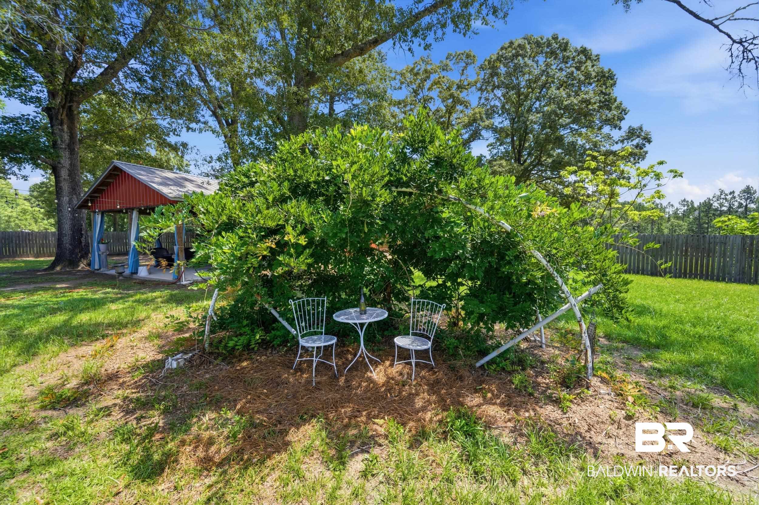 51620 Robert White Road Bay Minette, AL 36507 - Photo 75 of 81 Landscaped outdoor area featuring a red-roofed covered patio, mature trees, and a wooden privacy fence