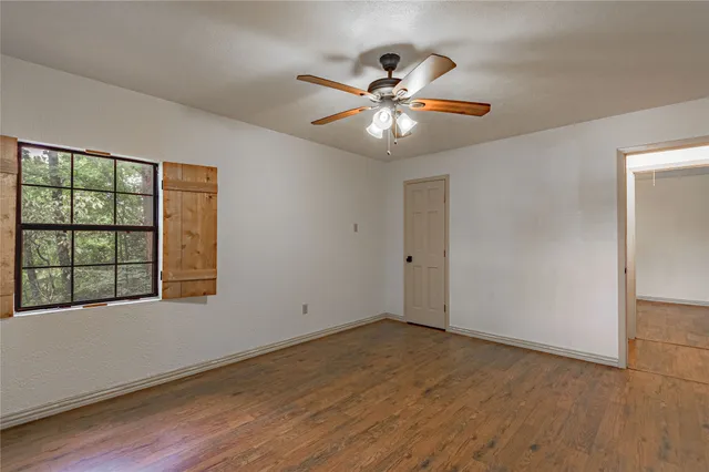 an empty room with wooden floor fan and windows