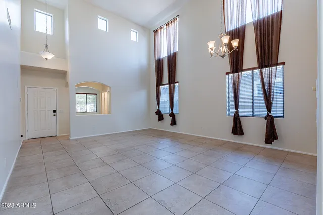 an empty room with chandelier fan and windows