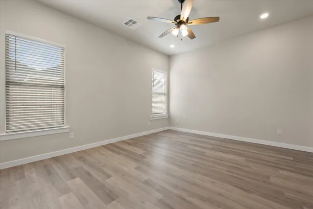 an empty room with wooden floor fan and windows
