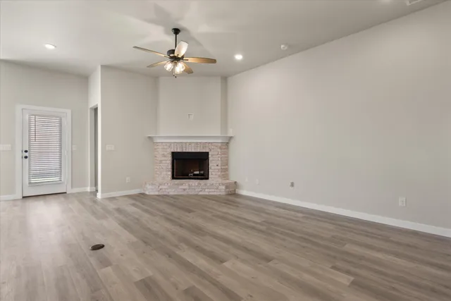 an empty room with wooden floor a ceiling fan a fireplace and windows