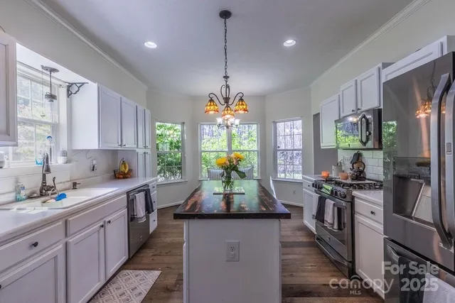 a kitchen with kitchen island granite countertop stainless steel appliances a stove oven a sink a refrigerator white cabinets and wooden floor