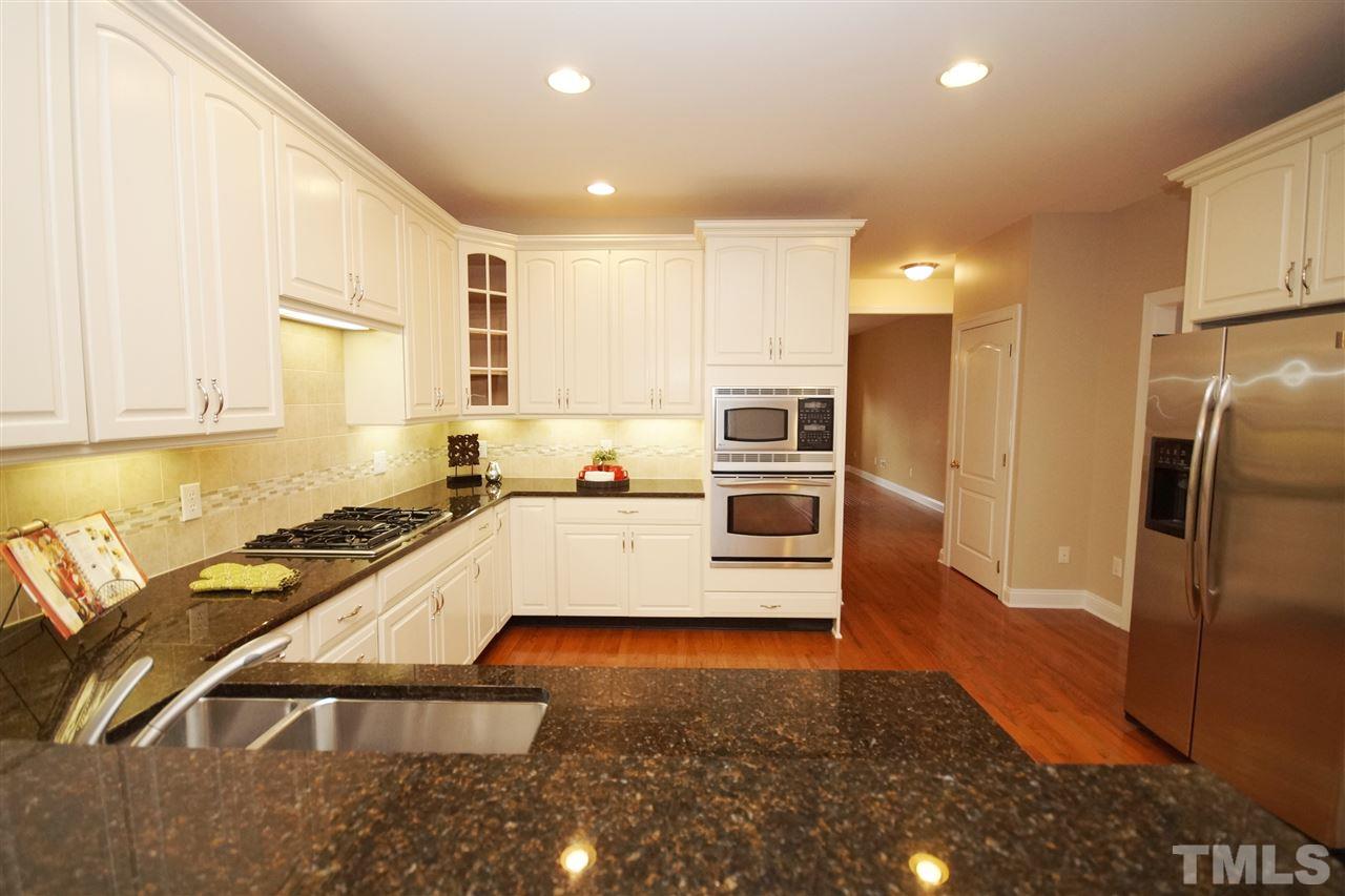 11032 Fair Chase Court Raleigh, NC 27617 - Photo 13 of 25 a large kitchen with stainless steel appliances a large counter top a stove a refrigerator and white cabinets