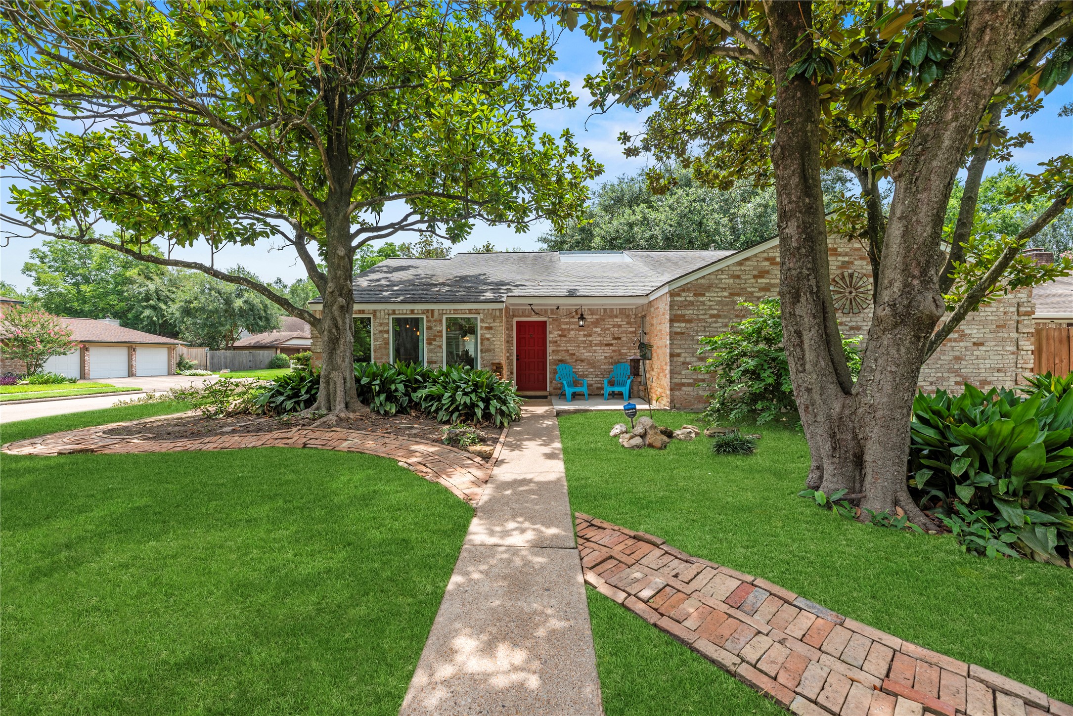 14203 Wickersham Lane Houston, TX 77077 - Photo 2 of 25 A bright, daytime look at the front entrance highlighting the covered entryway, expansive front windows that invite abundant natural light, and a winding brick path accenting the lush green yard.