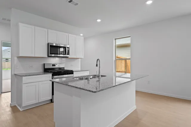 a kitchen with stainless steel appliances granite countertop a sink a stove a microwave a refrigerator a window and white cabinets