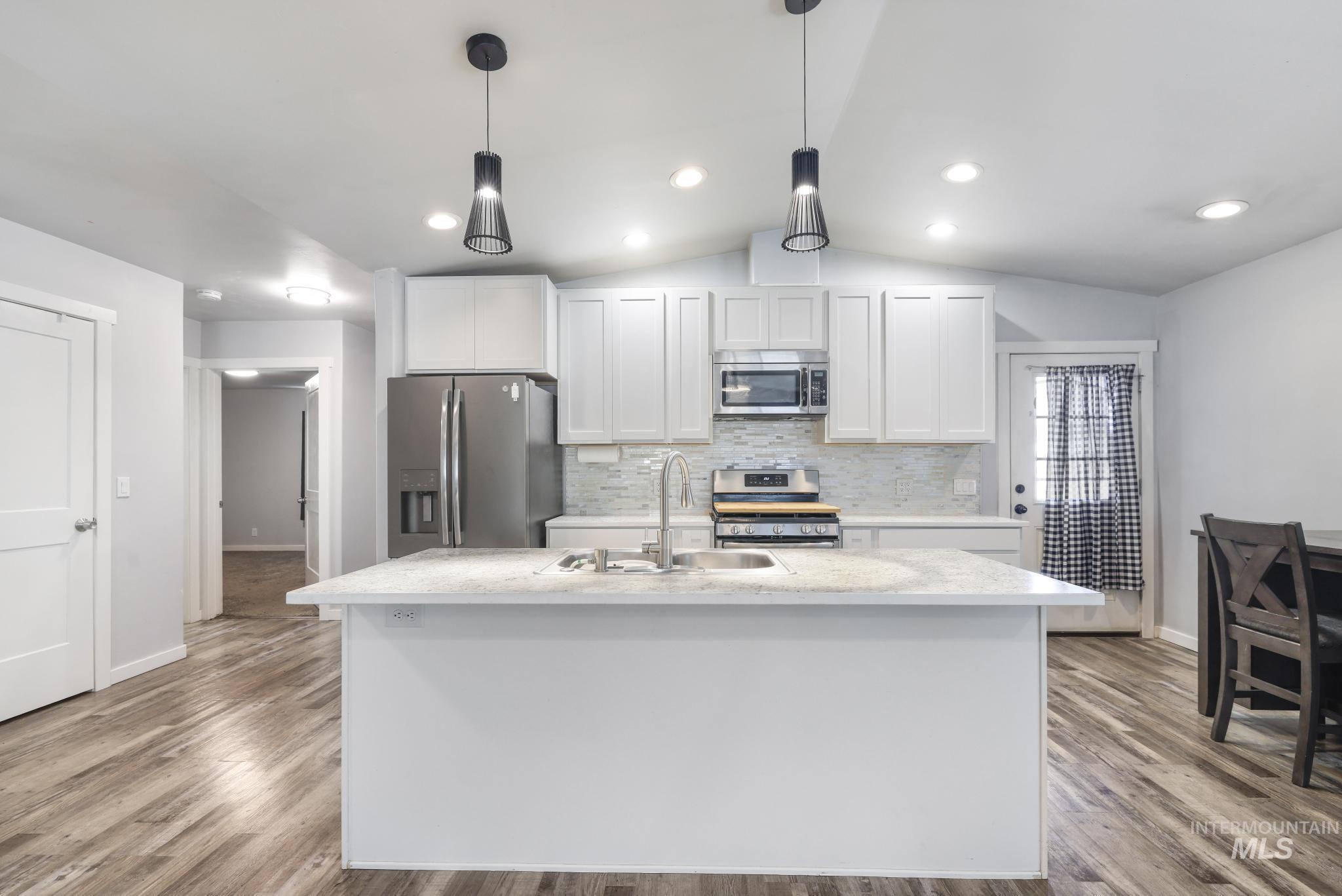 826 Normal Burley, ID 83318 - Photo 7 of 21 Kitchen featuring a spacious island with an undermount sink, white shaker cabinetry, stainless steel appliances, and wood-finish flooring