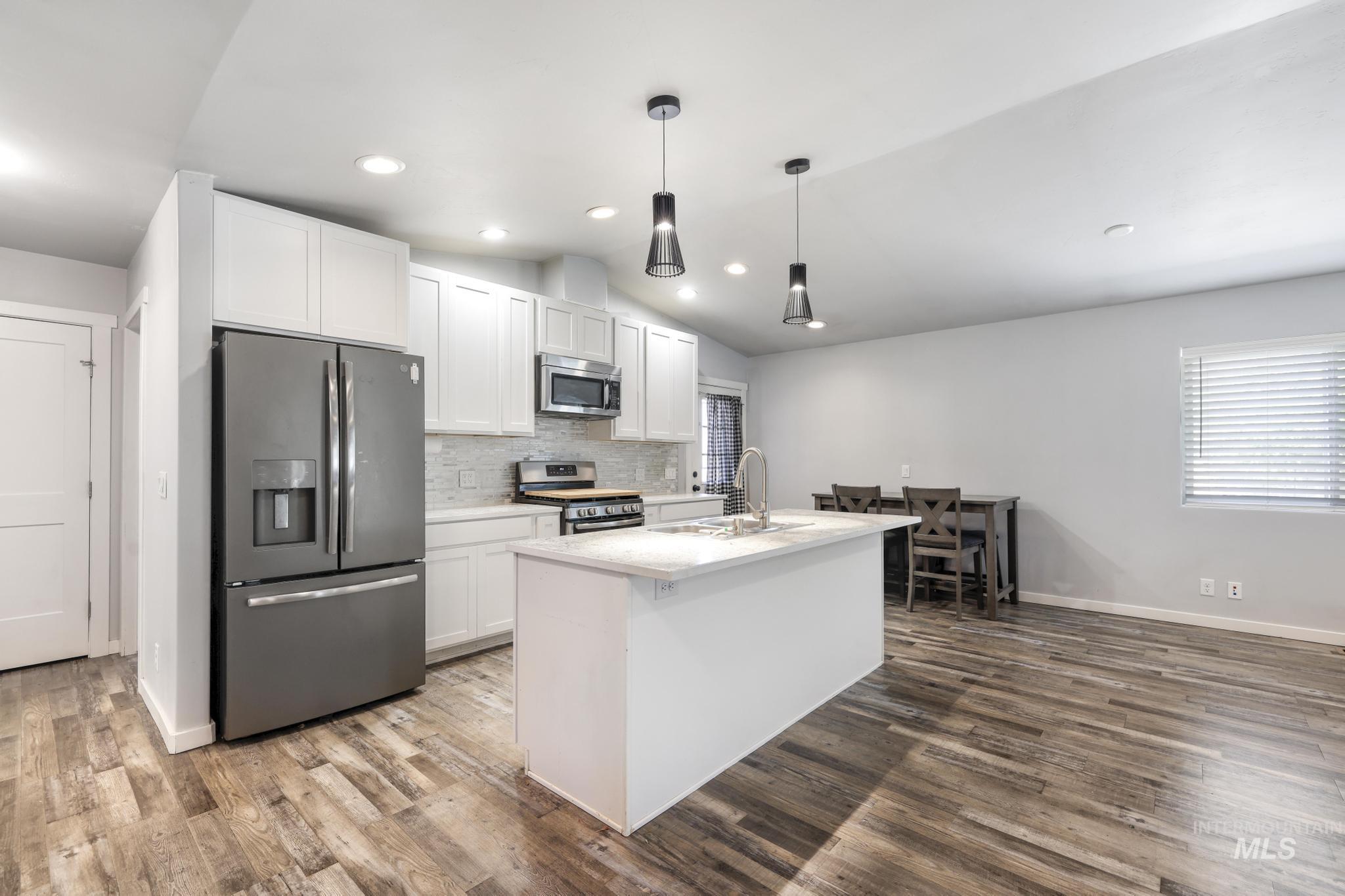 826 Normal Burley, ID 83318 - Photo 8 of 21 Open-concept kitchen featuring an island with an integrated sink, stainless steel appliances, white cabinetry, and wood-finish flooring