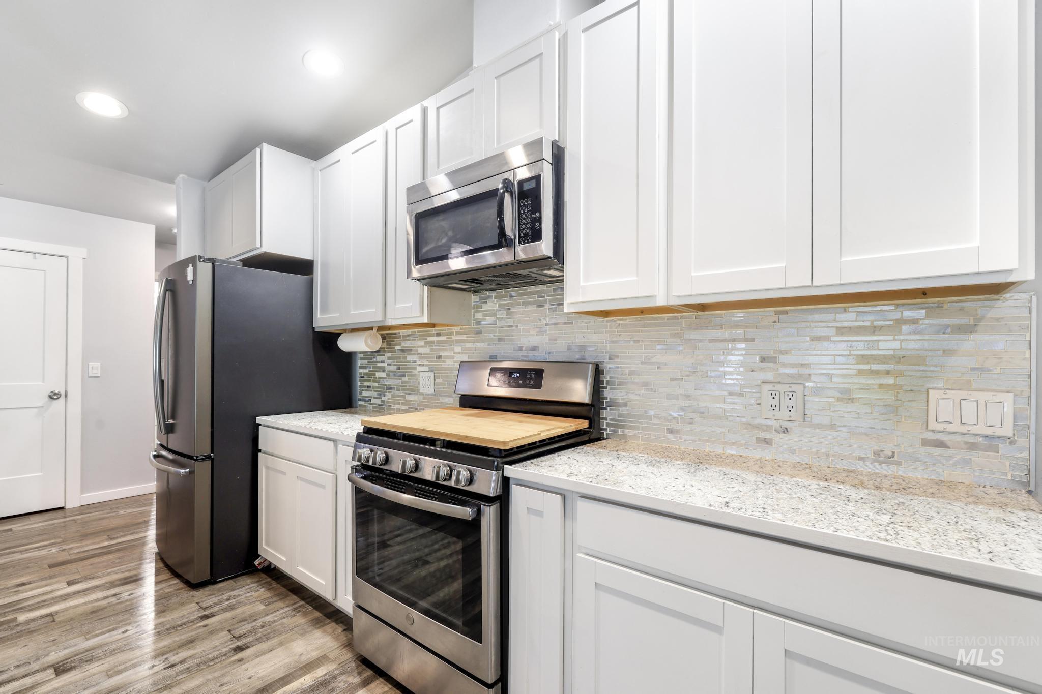 826 Normal Burley, ID 83318 - Photo 9 of 21 Modern kitchen featuring white shaker cabinetry, stainless steel appliances, granite-style countertops, mosaic tile backsplash, and wood-finish flooring