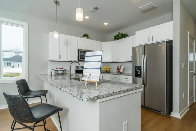 a kitchen with kitchen island granite countertop a counter space a refrigerator a sink and chairs