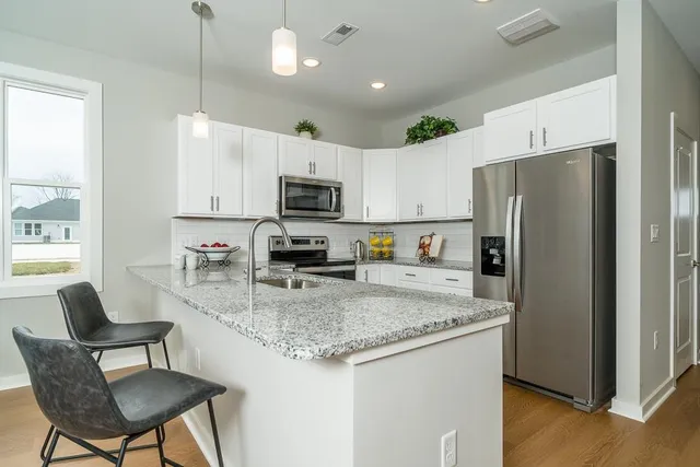 a kitchen with kitchen island granite countertop a refrigerator a stove a sink a dining table and chairs