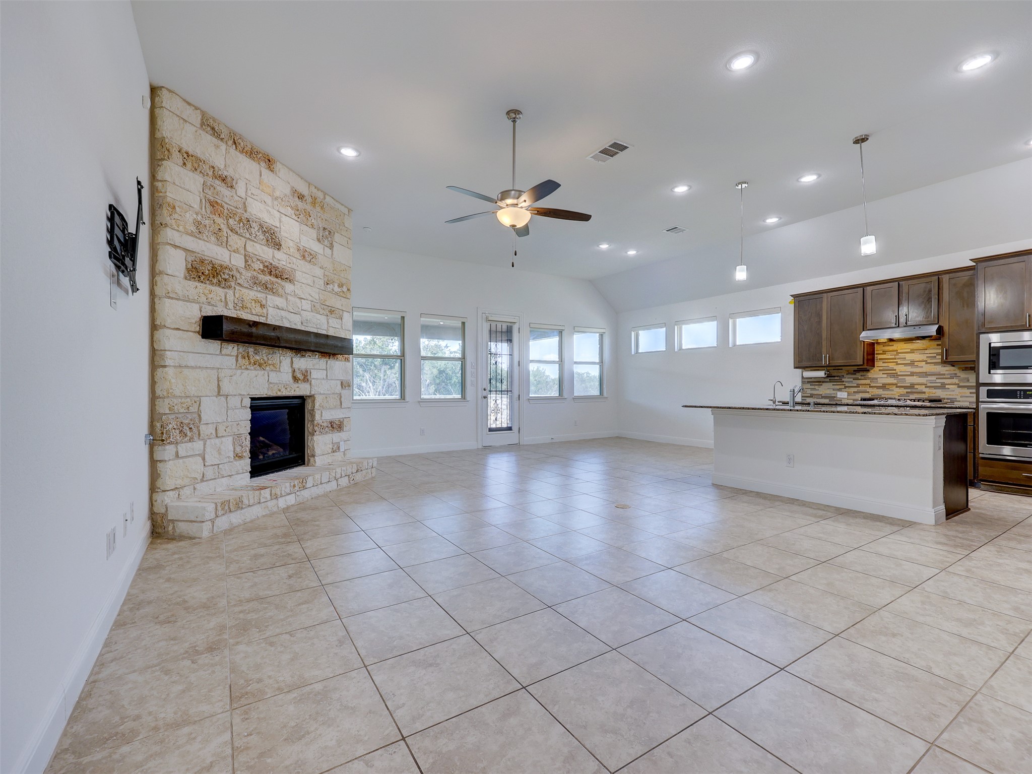 2020 Base Burner Path Leander, TX 78641 - Photo 5 of 22 Unfurnished living room with light tile patterned flooring, a stone fireplace, vaulted ceiling, a ceiling fan, and recessed lighting
