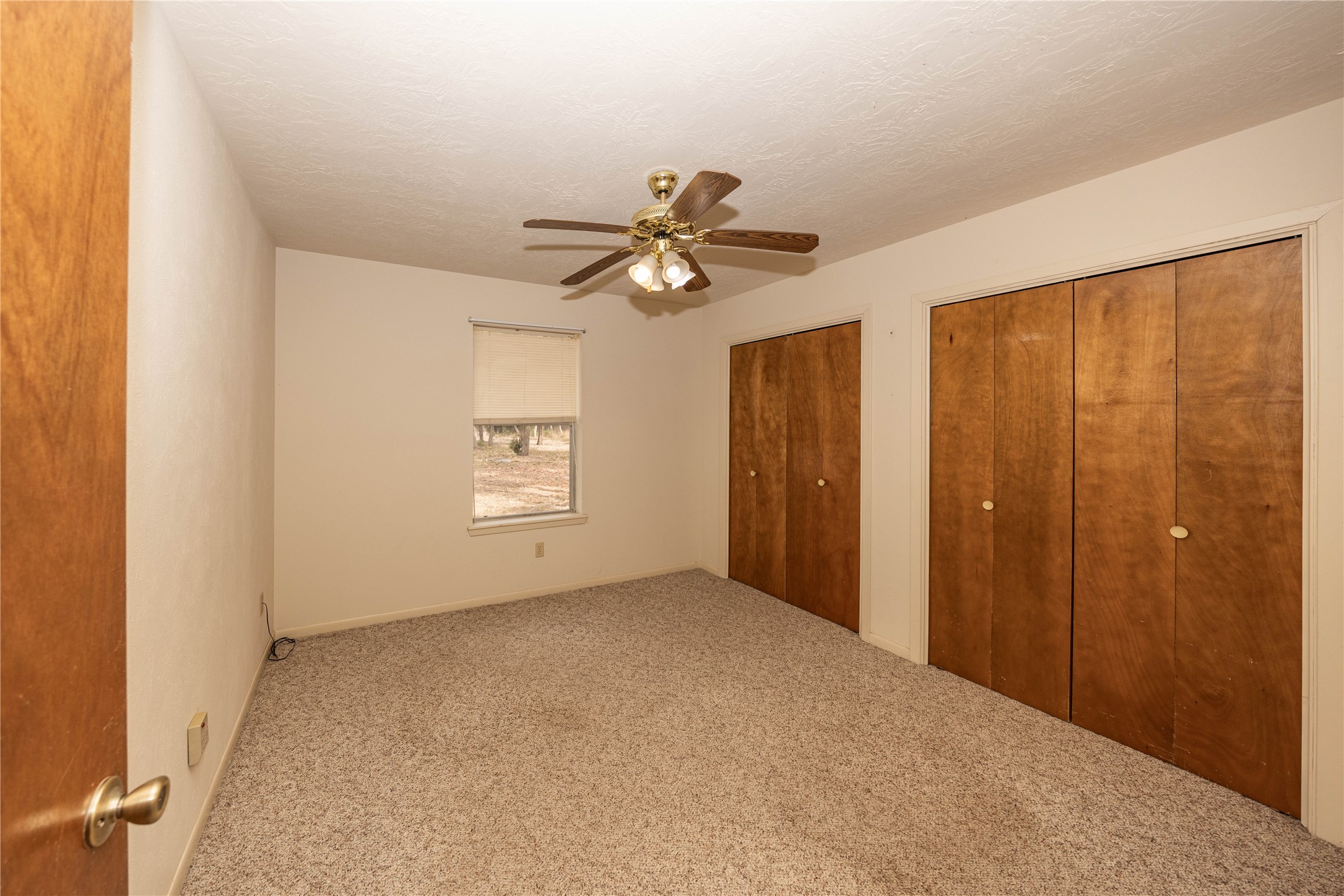 2501 Fischer Store Road Wimberley, TX 78676 - Photo 10 of 23 Neutral-toned room featuring a window with a roller shade, light-colored textured carpeting, and two sets of bi-fold closet doors