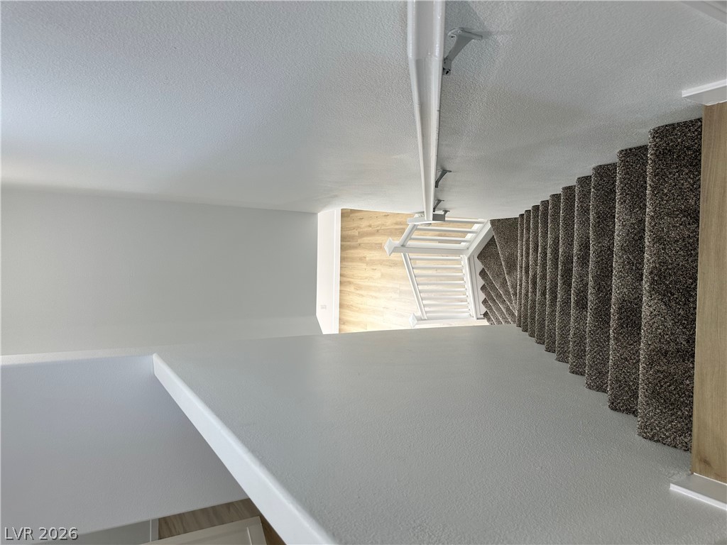 9639 West Post Road Las Vegas, NV 89148 - Photo 12 of 30 Carpeted stairs descend toward a light-filled lower landing featuring smooth hardwood flooring.