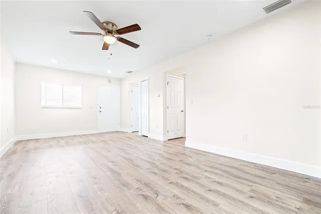 an empty room with wooden floor ceiling fan and windows