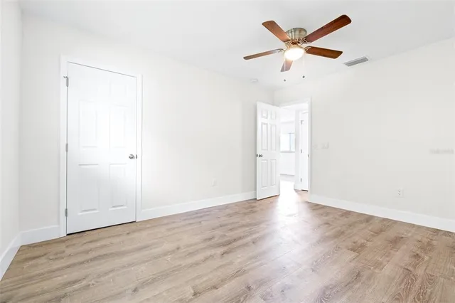 an empty room with wooden floor ceiling fan and window
