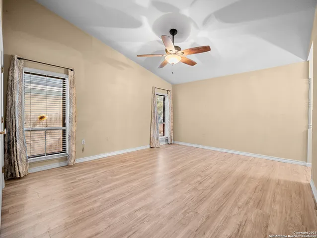 an empty room with wooden floor chandelier fan and windows