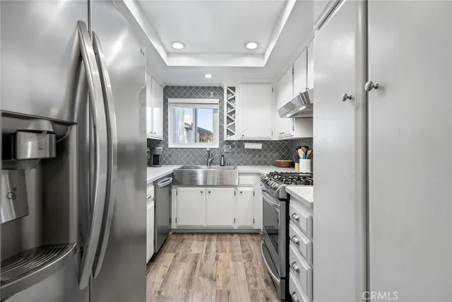 a kitchen with stainless steel appliances granite countertop a refrigerator a sink a stove and white cabinets with wooden floor