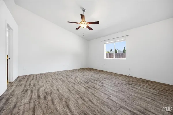 an empty room with wooden floor ceiling fan and windows