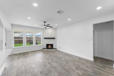 a view of an empty room with wooden floor a fireplace and a window