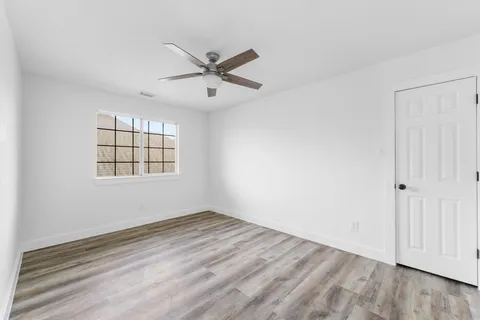 an empty room with wooden floor fan and windows