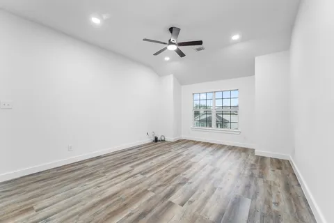 an empty room with wooden floor ceiling fan and windows