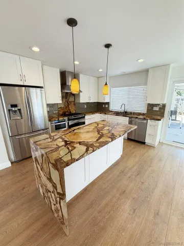 a large kitchen with kitchen island a stove a refrigerator a sink dishwasher a oven and a dining table with wooden floor