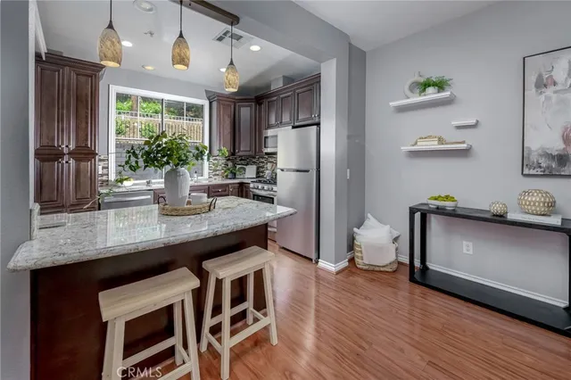 a kitchen with stainless steel appliances granite countertop a stove a refrigerator a sink a dining table and chairs with wooden floor