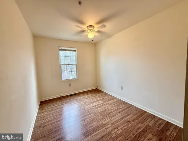 an empty room with wooden floor fan and windows