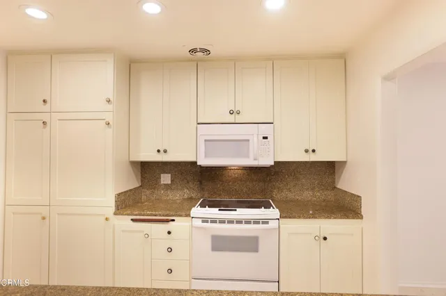 a kitchen with granite countertop white cabinets and white stove