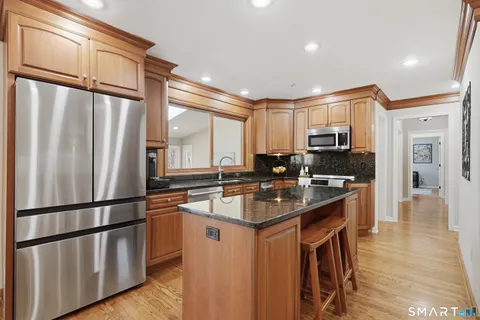 a kitchen with stainless steel appliances granite countertop a refrigerator a sink dishwasher a stove and a refrigerator with wooden floor