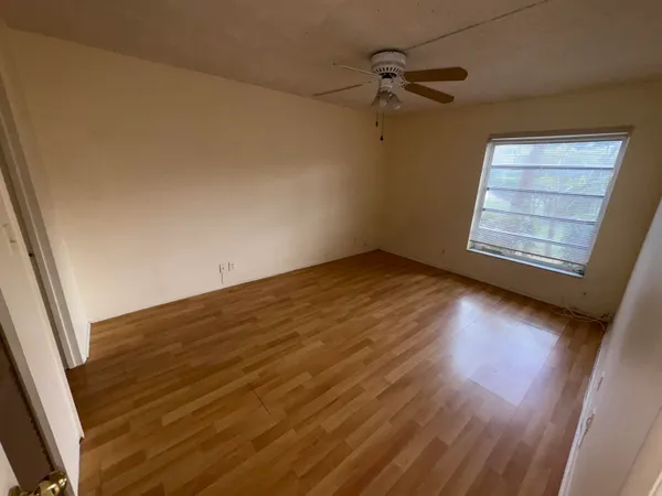 an empty room with wooden floor fan and windows