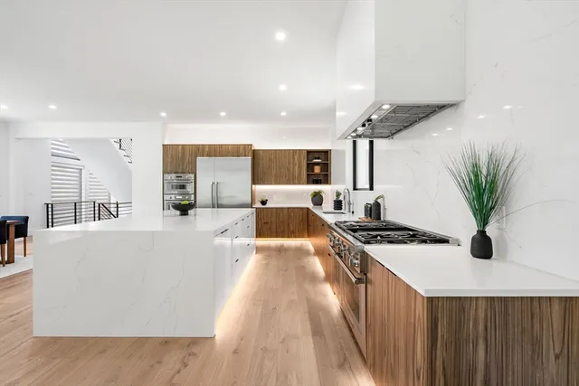 a large white kitchen with stainless steel appliances a large counter top a stove a chimney a sink and a refrigerator