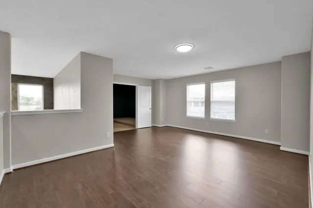 a view of empty room with wooden floor and kitchen