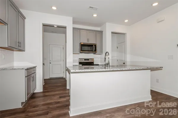 a kitchen with granite countertop a stove top oven a sink a refrigerator and white cabinets with wooden floor