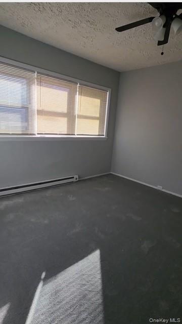 488 Nassau Road, Unit 2 Roosevelt, NY 11575 - Photo 2 of 2 Empty room with dark colored carpet, a baseboard radiator, a textured ceiling, and ceiling fan