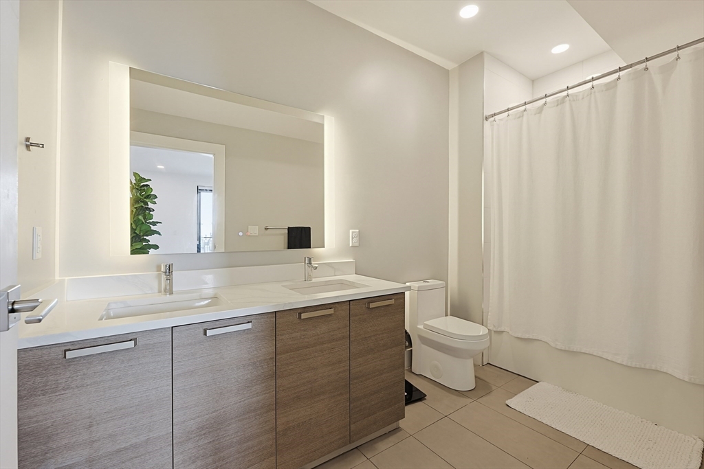 30 Penniman Road, Unit 605 Boston, MA 02134 - Photo 8 of 19 a bathroom with a double vanity sink toilet and a mirror
