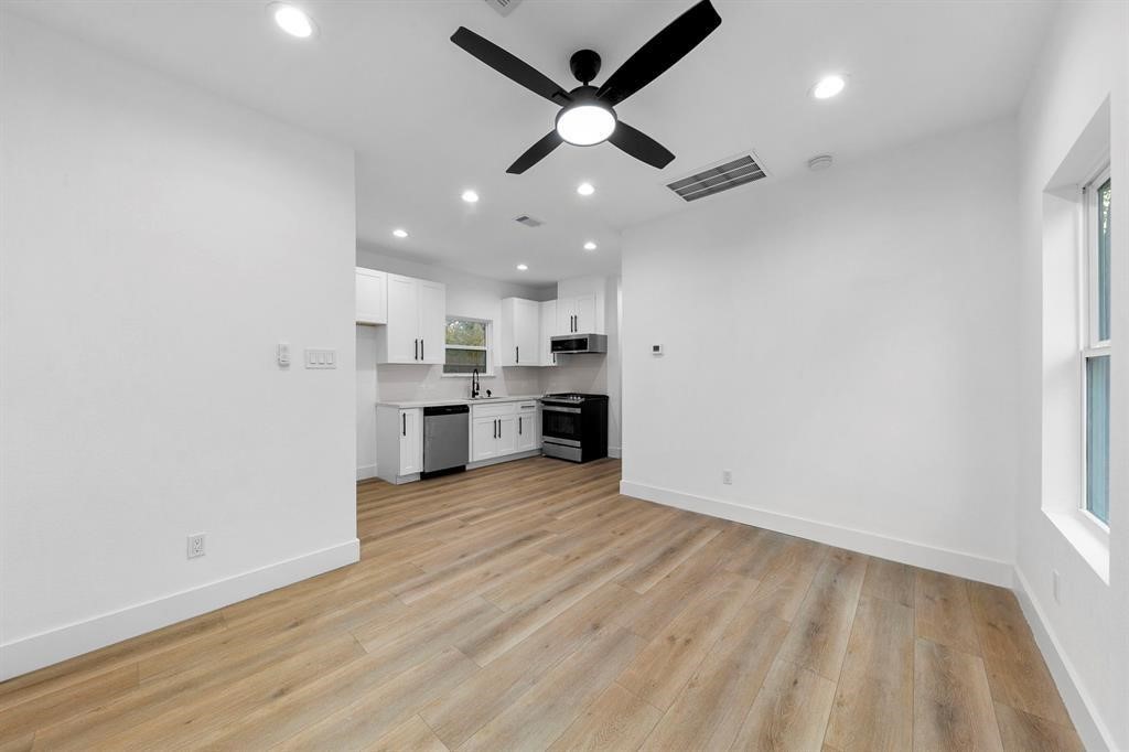 2805 Nettleton Street Houston, TX 77004 - Photo 5 of 9 This photo shows a bright, modern open-concept living area with a sleek kitchen. It features wood-look flooring, white cabinetry, stainless steel appliances, and a ceiling fan. The space is well-lit with recessed lighting and a window providing natural light.